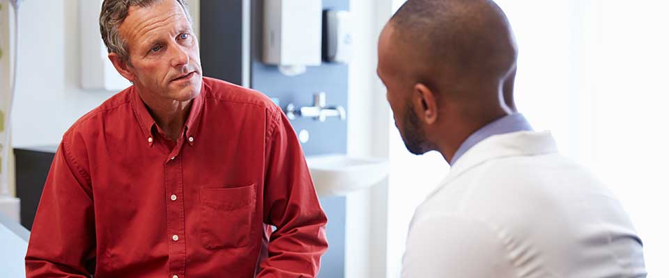 A man in a red button-up shirt discusses his health with his primary care doctor.